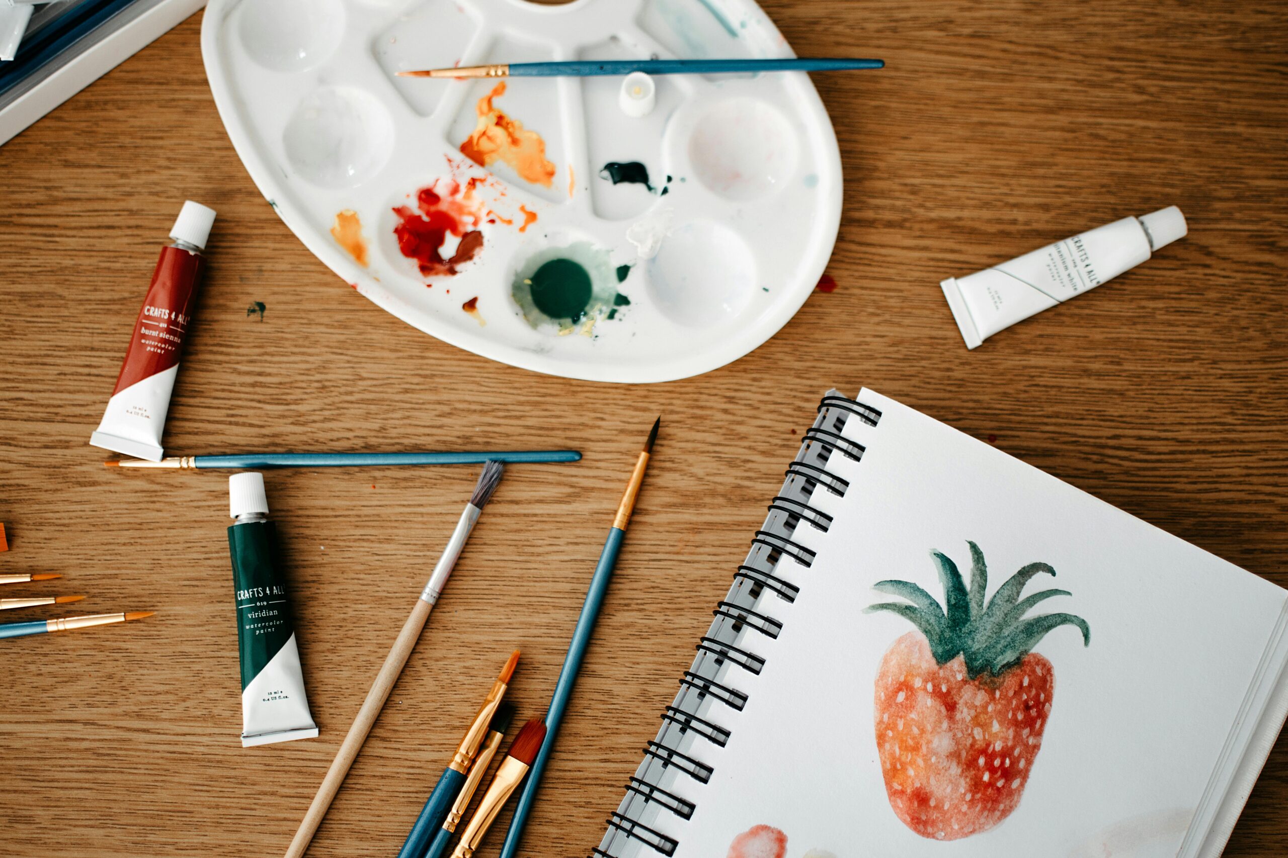 Explore a vibrant creative art space with watercolors and brushes on a wooden desk.