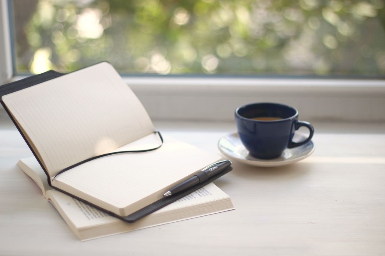 A quiet writing desk with a single ceramic cup and an open notebook — the visual of a discipline that returns rather than one that never breaks.
