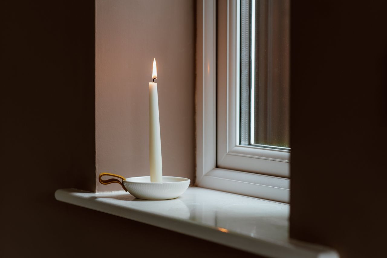 A quiet windowsill with a taper candle and a small ceramic bowl in morning light — the visual of a ritual small enough to keep.