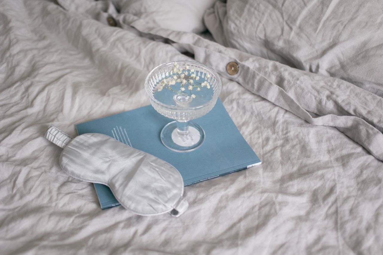 A soft afternoon still life — a glass of water, a book, a linen throw across a chair — the visual of wellness distributed across a whole day rather than compressed into one hour.