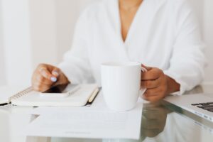 A pair of hands cradling a mug at the edge of an open notebook — the visual of a familiar place stretched, gently, one page further.