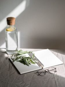 A soft still life on a kitchen counter — a glass of water, a folded linen napkin, an open notebook, late afternoon light — the visual of a body being cared for through a season of change.